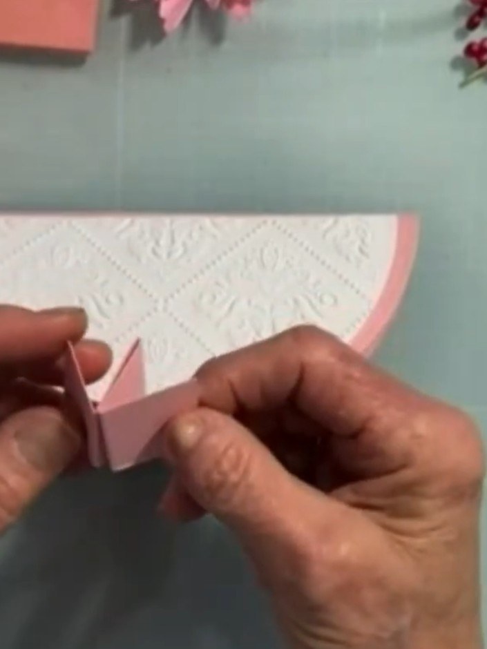 Step 13: Score a 1 x 4 inch strip of pink cardstock at 1 inch, 2 inch and 3 inch intervals. Fold the strip into a W-sha