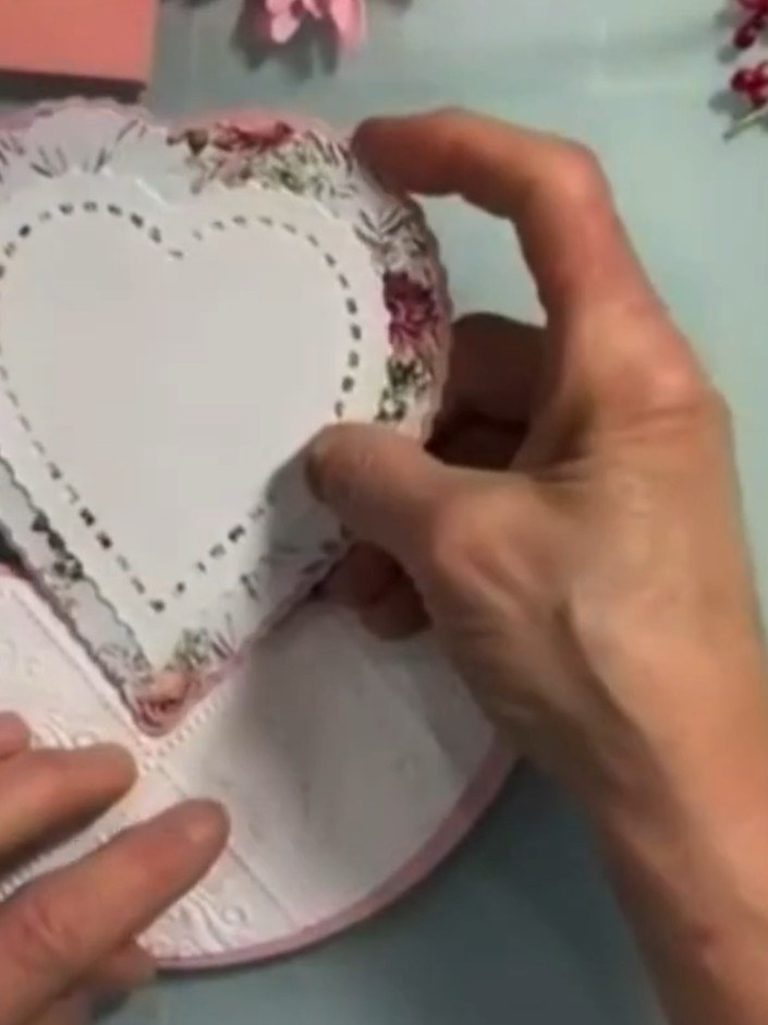 Step 16: Attach the completed heart-shaped floral topper to the top section of the rocker card base, positioning it cen