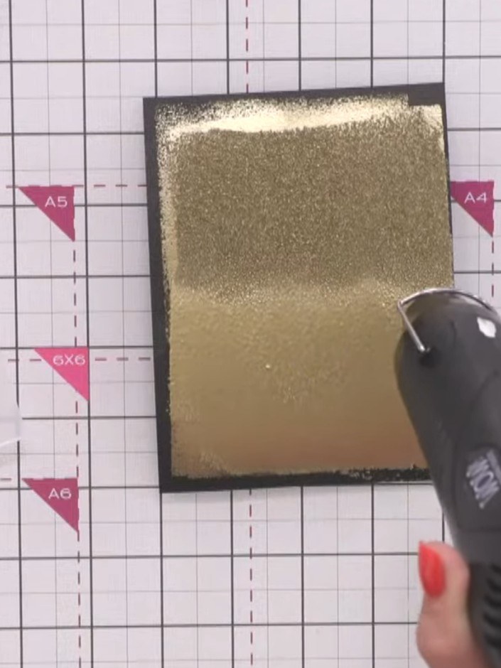 Step 11: Abre la carpeta de embossing con cuidado para descubrir el efecto dorado en bajorrelieve sobre la cartulina negra.