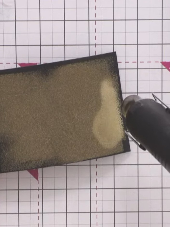 Step 7: Using the heat gun, apply heat to the embossing powder until it melts and creates a metallic gold finish on th
