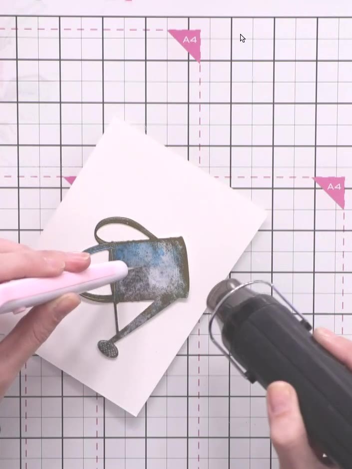 Step 14: Heat set the embossing powder using a heat gun, holding the watering can steady with tweezers. Move the heat g