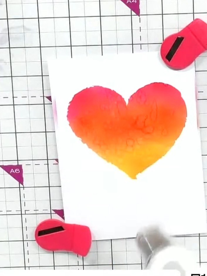 Step 5: Carefully lift and remove the stencil from the card to reveal the ombré heart design. Allow the ink to dry sli