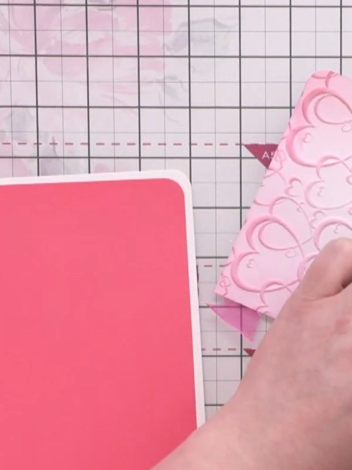 Step 11: Troquela un corazón en cartulina rosa y pégalo sobre el nudo del listón con cojines de espuma (pads 3D) para darle volumen.