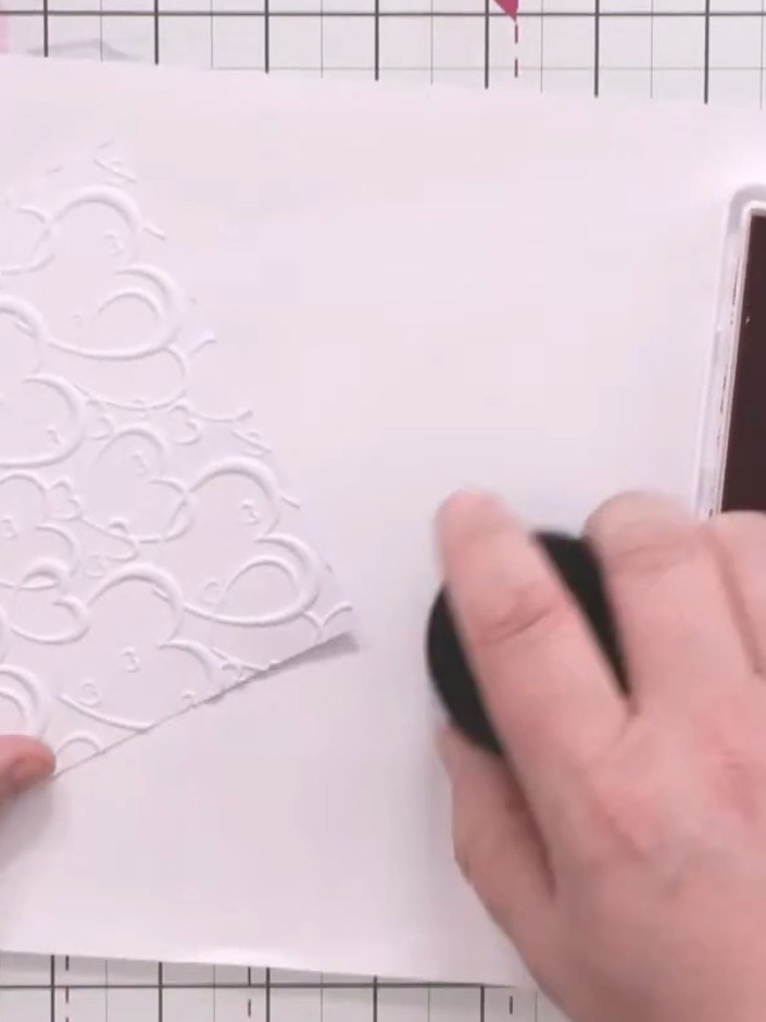 Step 4: Using a large blending brush, dust magenta ink over the embossed hearts in circular motions. This will bring o
