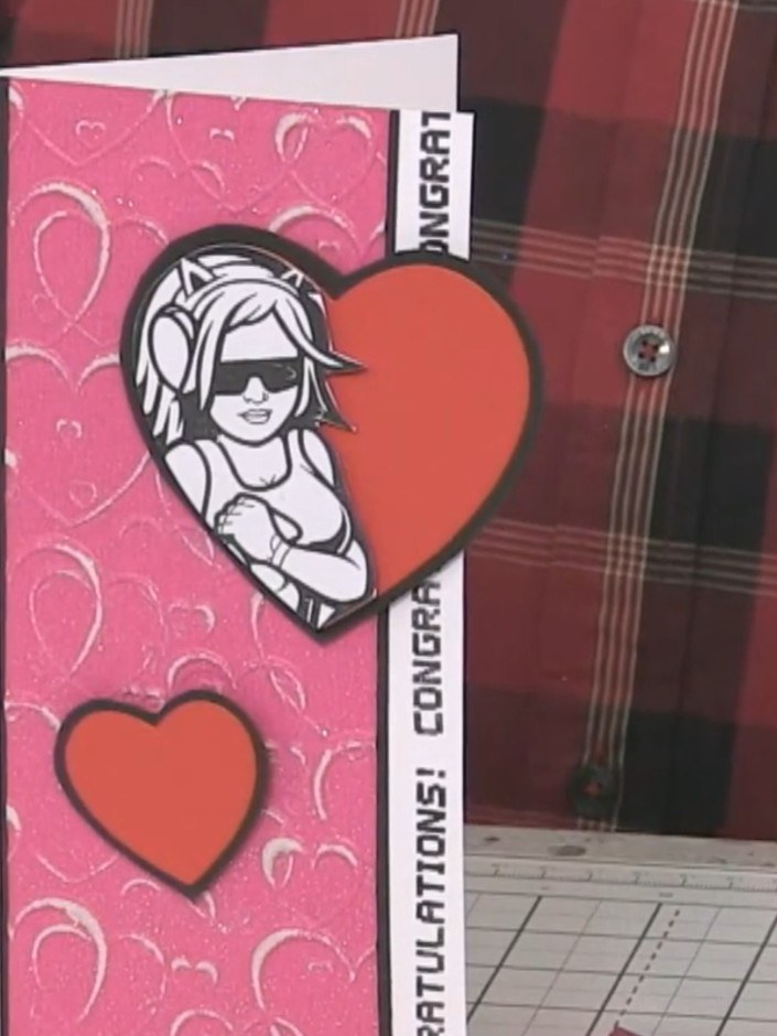 Step 16: Layer the smaller coral heart onto the card front using a foam pad to add depth. Position it below the charact