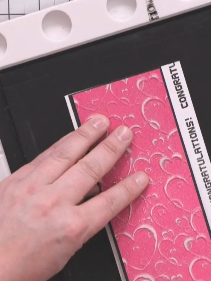 Step 8: Adhere the embossed and sanded pink panel to the black card base using glue, positioning it slightly towards t