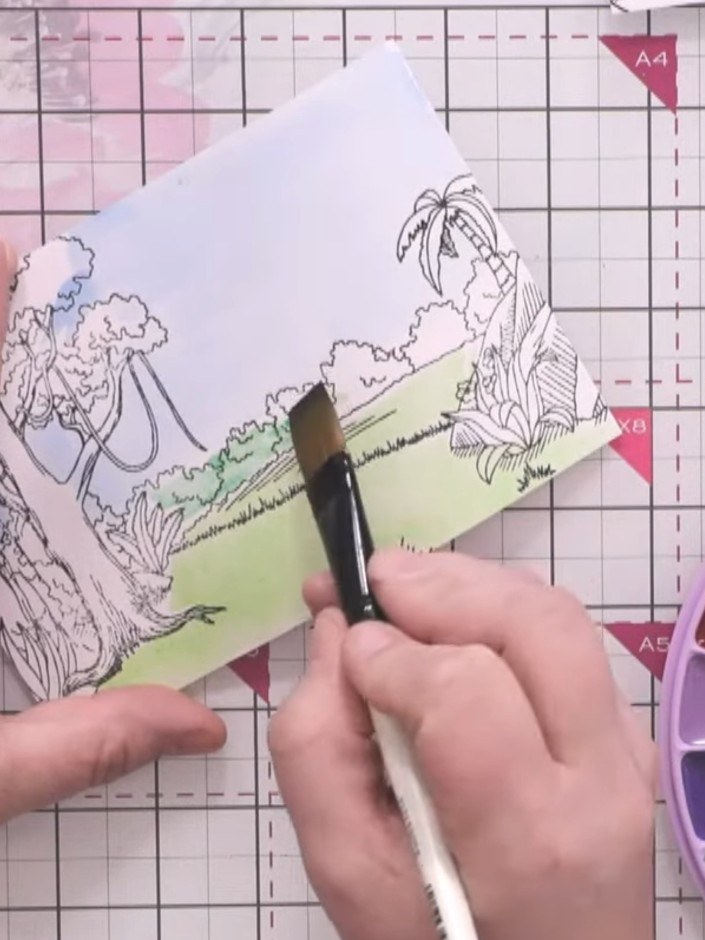 Step 6: Using a larger brush, add darker greens and browns to the tree lines and rocks on your stamped image. Keep you