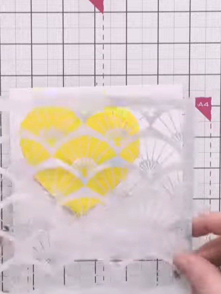 Step 3: Position the yellow paper heart mask over the fan stencil pattern on your white card front. Secure it lightly 