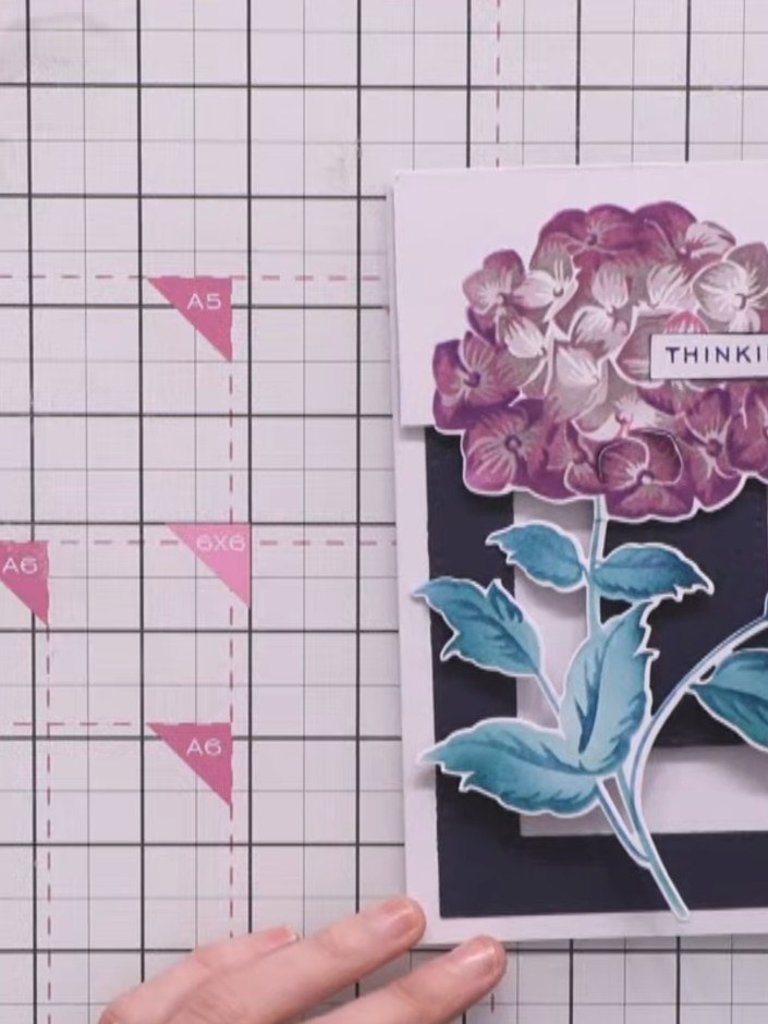 Step 9: Adhere the 'THINKING OF YOU' sentiment to the top of the purple hydrangea flower using foam pads or adhesive. 