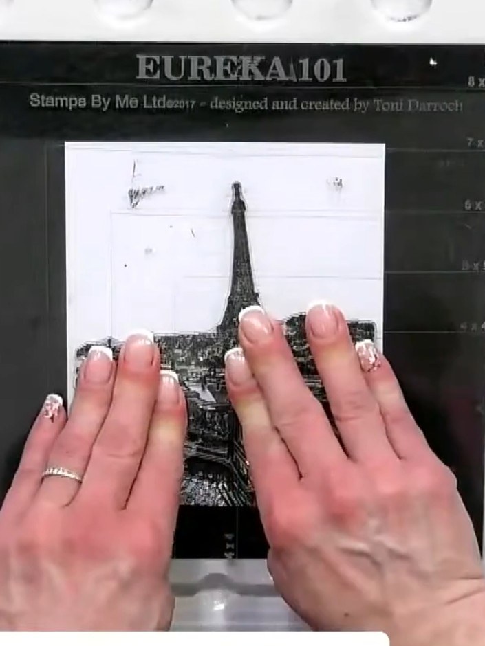 Step 4: Position the Paris skyline stamp over the masked figure area and stamp it onto the white card, ensuring the fi