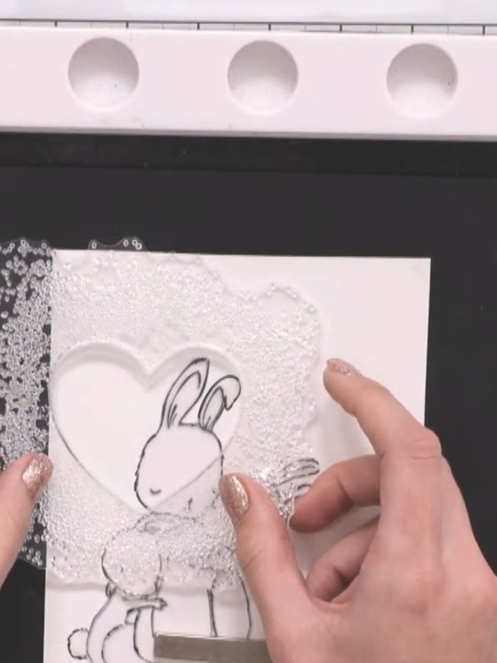 Step 4: Stamp a large decorative frame or heart stamp over the masked bunny image, positioning it to frame the design.