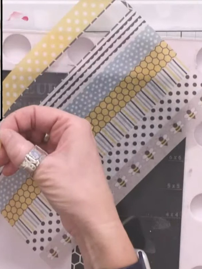 Step 5: Assemble your card by positioning the washi tape strips to frame the stamped bee background. Ensure the strips