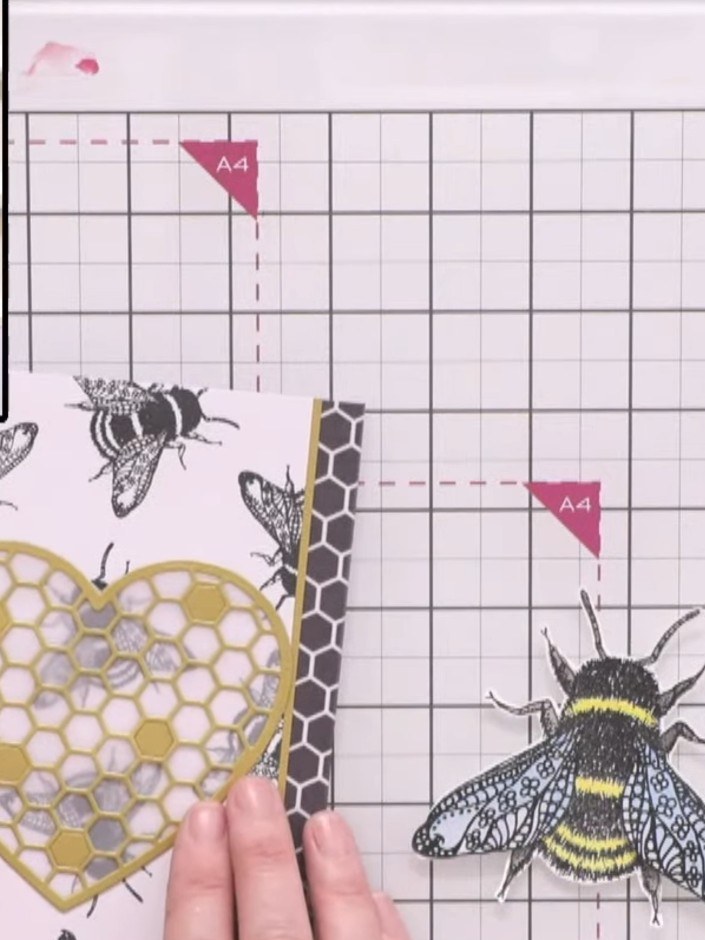 Step 6: Position the gold honeycomb heart die-cut over the stamped bee background, ensuring the vellum backing is behi