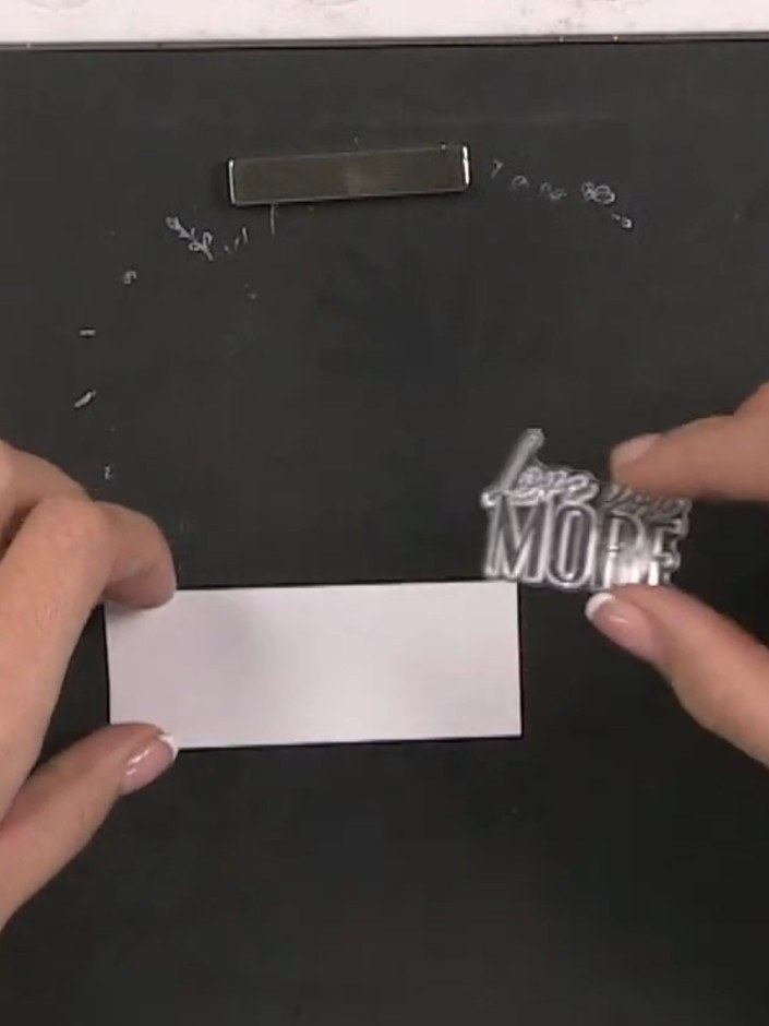Step 10: Stamp a sentiment onto a white card strip using a stamp from the set. Position the 'Love You More' sentiment c