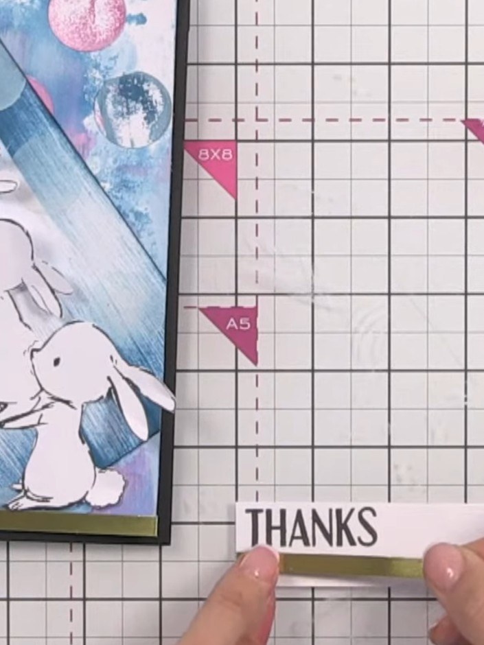 Step 13: Stamp 'THANKS' onto the gold strip beneath the bunny panel. Use a glass mat to avoid the stamp clanging on the