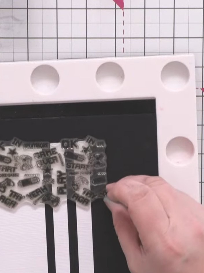 Step 11: Stamp the gaming-themed background images onto the decorative panels using black hybrid ink. Position the stam