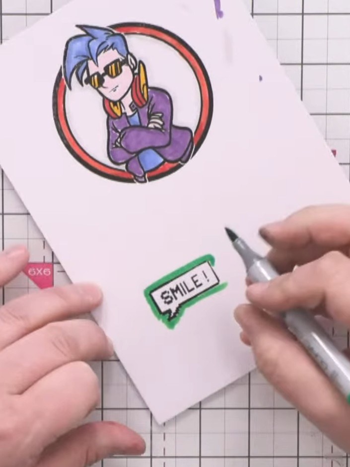 Step 10: Colour the border of the 'SMILE!' sentiment stamp with a green marker. Carefully cut out both the character ci