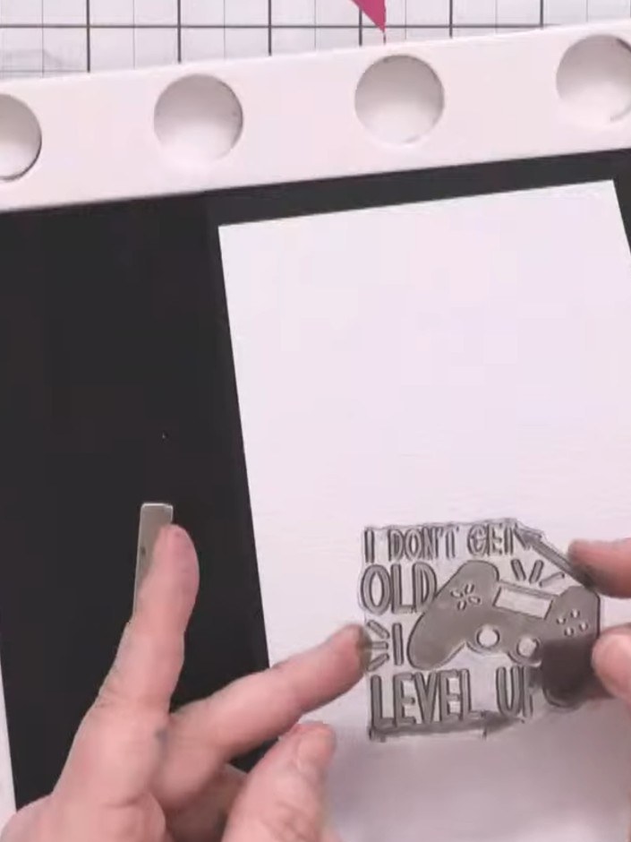 Step 9: Stamp the 'I don't get old, I level up' sentiment onto linen-effect card using black ink. Press firmly multipl