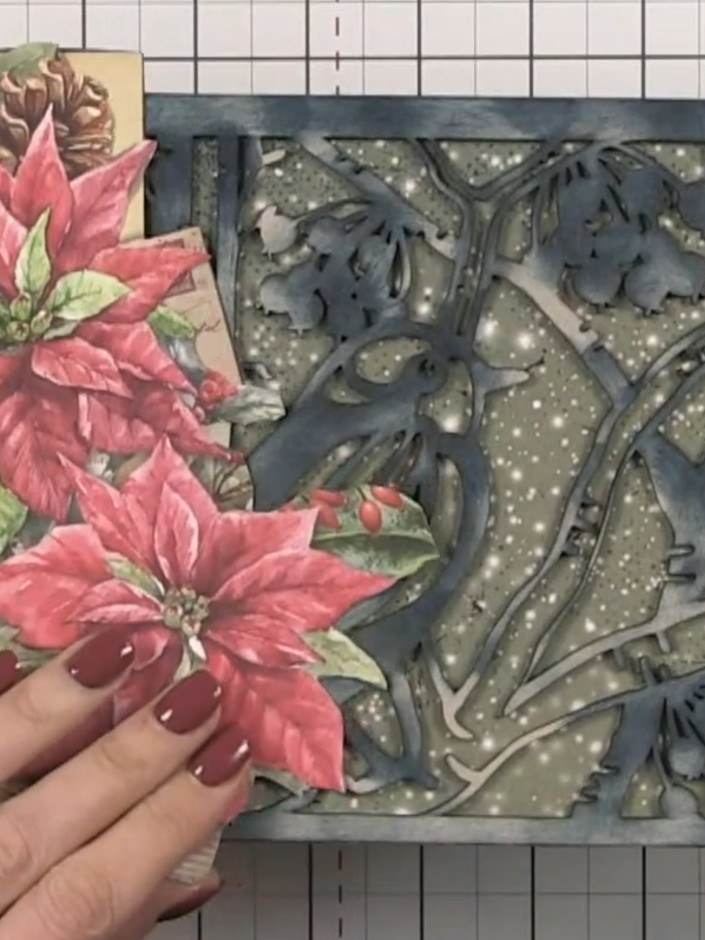 Step 7: Arrange the poinsettia embellishments, pine cones, and floral elements on the album cover, layering them over 