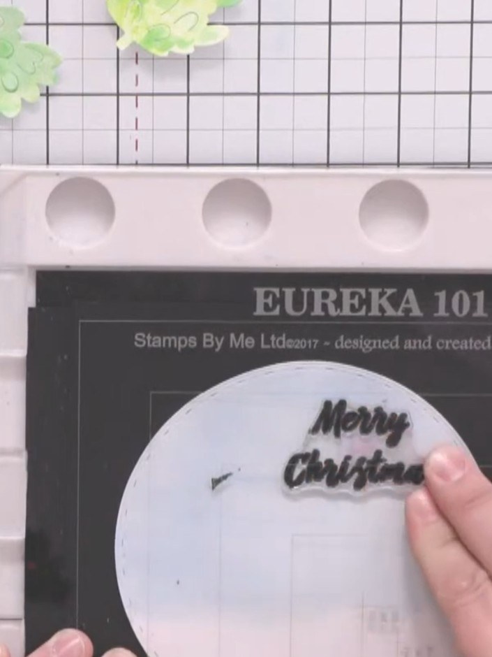 Step 15: Stamp a 'Merry Christmas' sentiment onto the white circular background using black ink, positioning it in the 