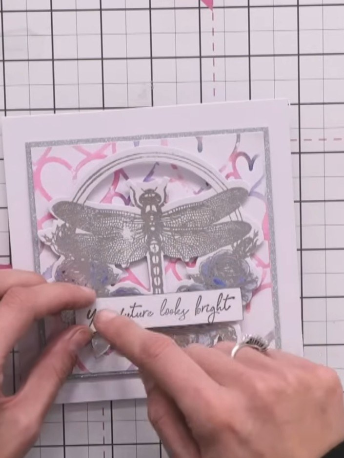 Step 14: Mount the sentiment strip onto the card using small foam pads, positioning it centrally below the dragonfly to