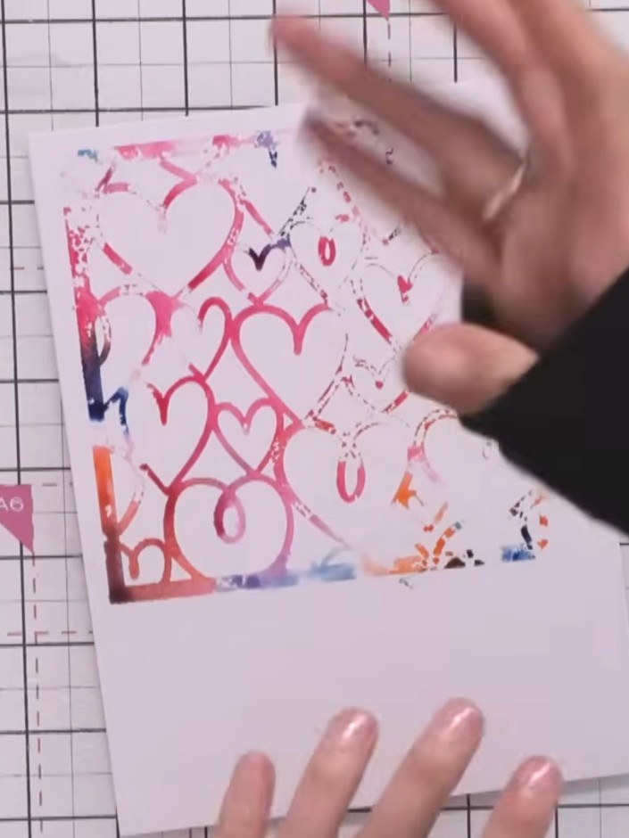 Step 8: Carefully lift the stencil away from the card to reveal the stamped and stencilled heart pattern. Allow the ba