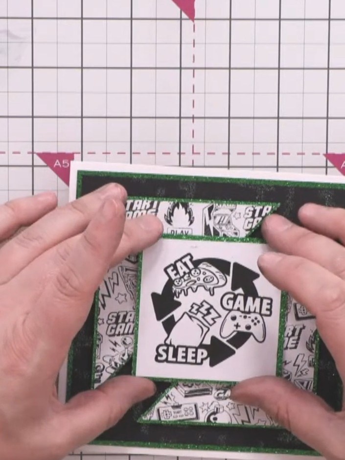 Step 13: Attach foam pads to the back of the central sentiment piece featuring the gaming controller design. Position i