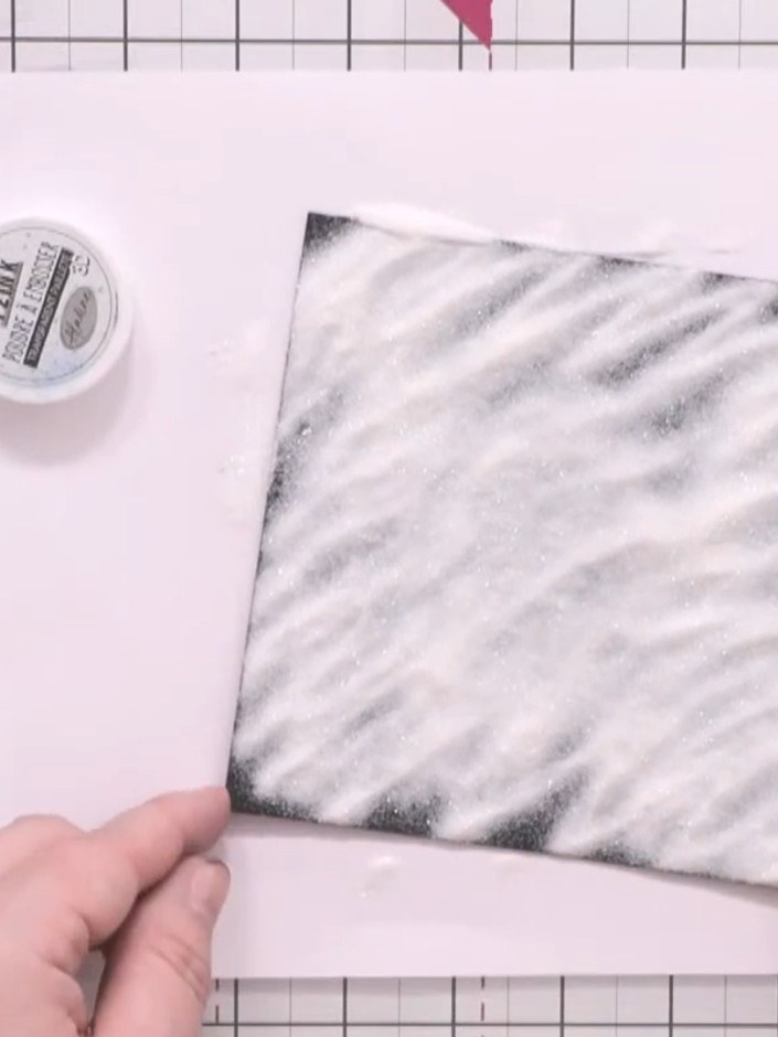 Step 5: Tip off the excess embossing powder from the black cardstock. Heat-set the remaining powder using a heat gun u