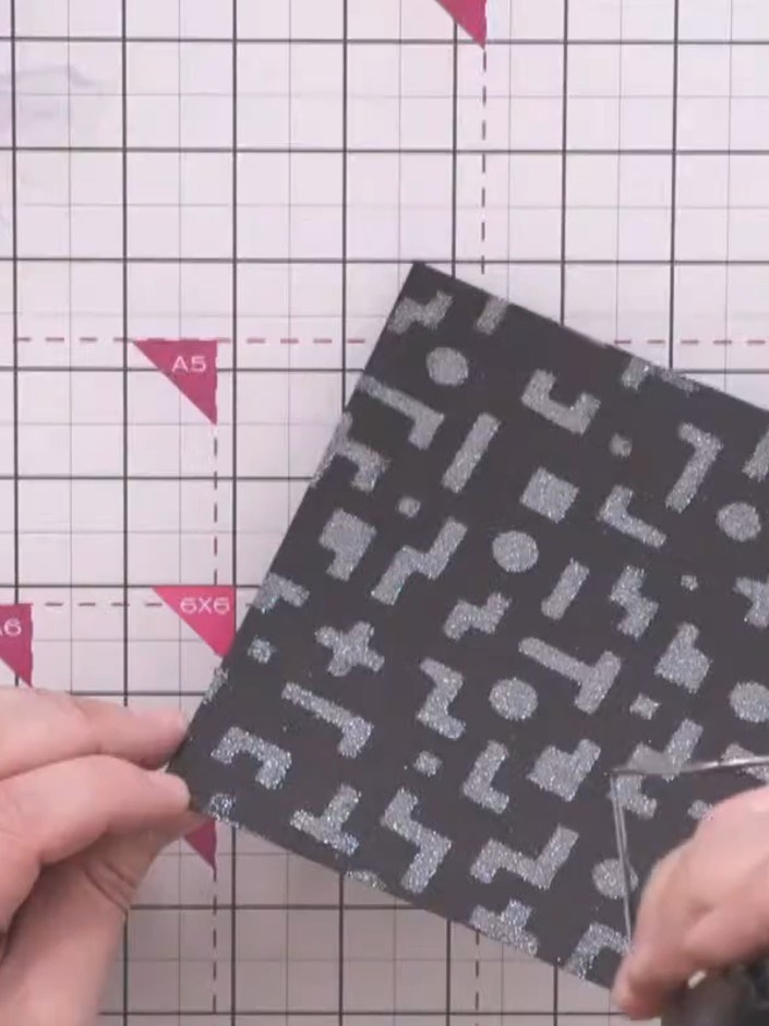 Step 6: Mount the embossed black panel onto iridescent green glitter cardstock using double-sided tape, leaving an eve