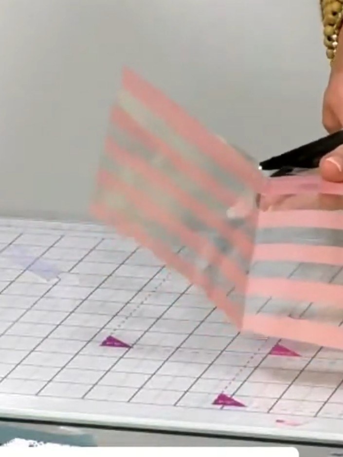 Step 10: Fold the top flap of the pink and grey striped acetate envelope down and secure it in place with adhesive to c