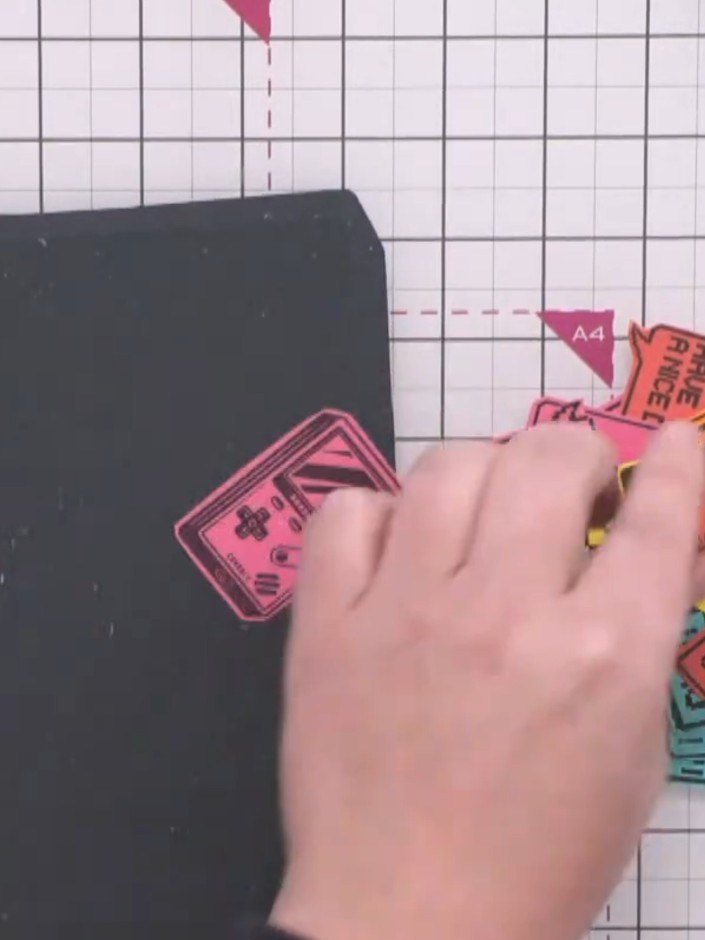 Step 7: Arrange the colourful stamped ticket pieces onto the dark grey background card. Position them in a scattered, 
