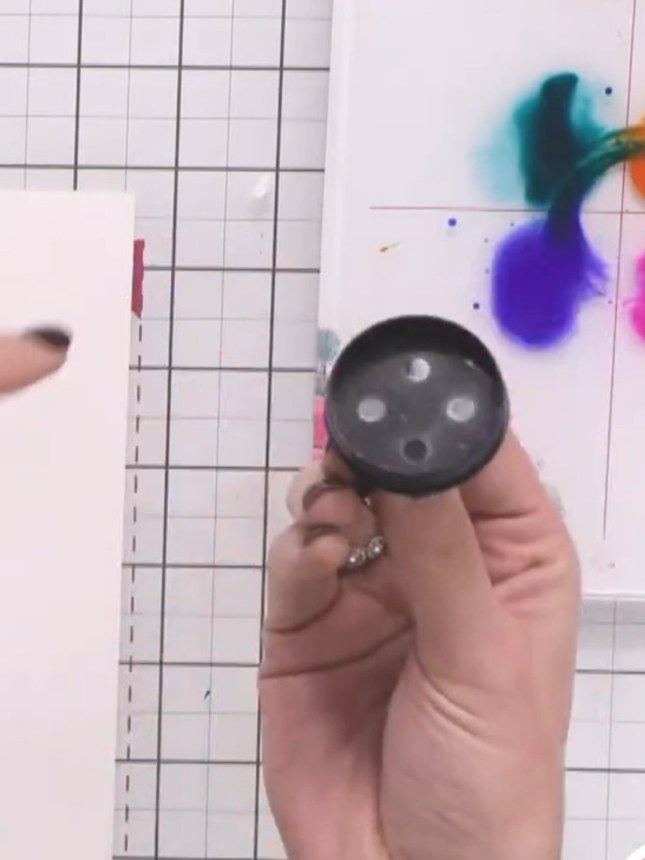 Passo 3: Dip the larger circular lid into one of the watercolour paints. Stamp it onto the watercolour card to create a