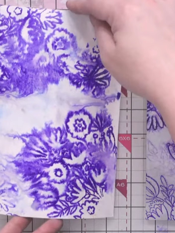 Passo 9: Position and glue the stamped purple foliage pieces onto your watercolour background. Arrange the blooms and f