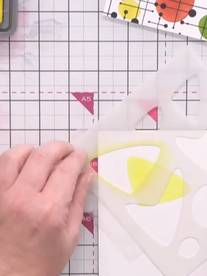 Stap 4: Apply turquoise distress oxide ink through a third geometric shape stencil, overlapping with the yellow and pi