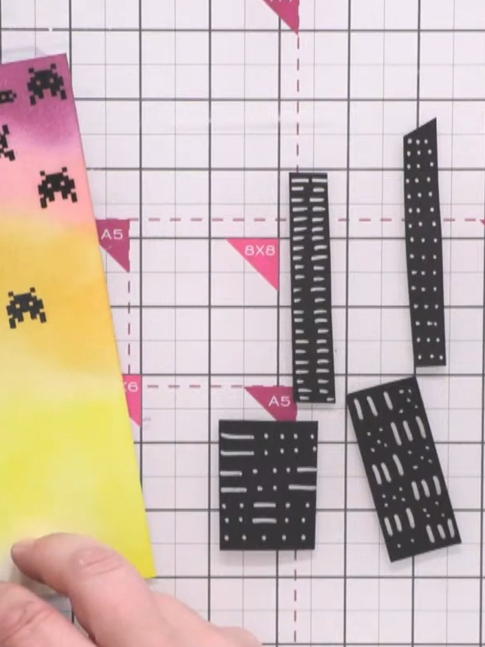 Passo 10: Glue the tallest building strips flat onto the card first as your back layer. Position them on the yellow and 