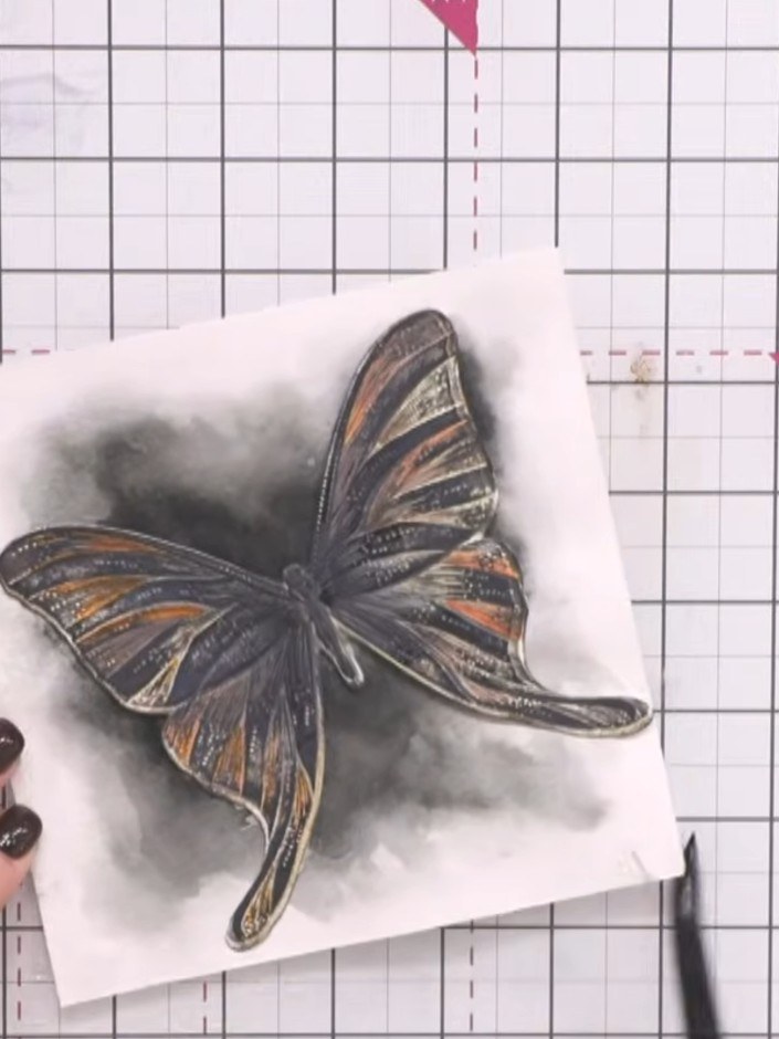 Passo 11: Position the completed butterfly onto your card base. The butterfly features dark grey and orange watercoloure