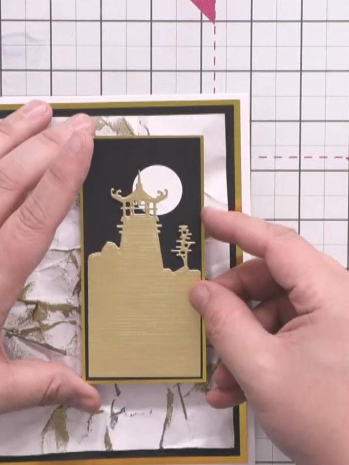 Stap 14: Position the gold pagoda die-cut at the top corner of the card, overlapping the black and white marble backgro