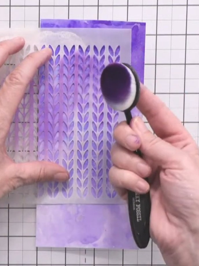 Step 7: Mount the inky background panel with the knitted pattern stencil design onto a dark purple card mat using a bl
