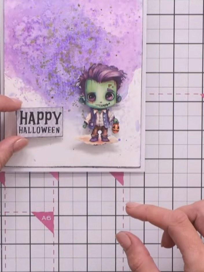 Step 16: Edge the 'Happy Halloween' sentiment stamp with black ink pad. Adhere the sentiment to the left side of the ca