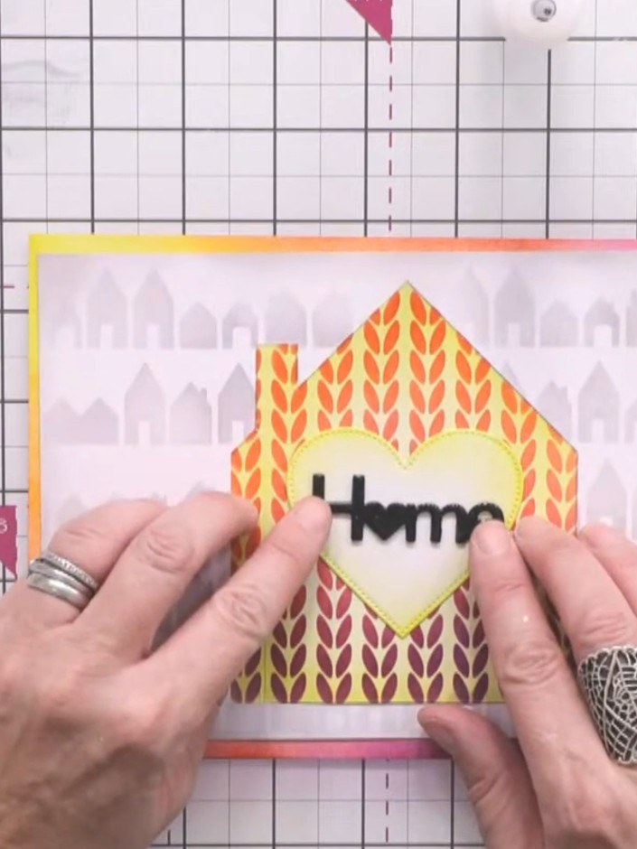 Step 11: Stamp the sentiment 'home' from the mini house stamp set onto the yellow heart aperture using black ink and th