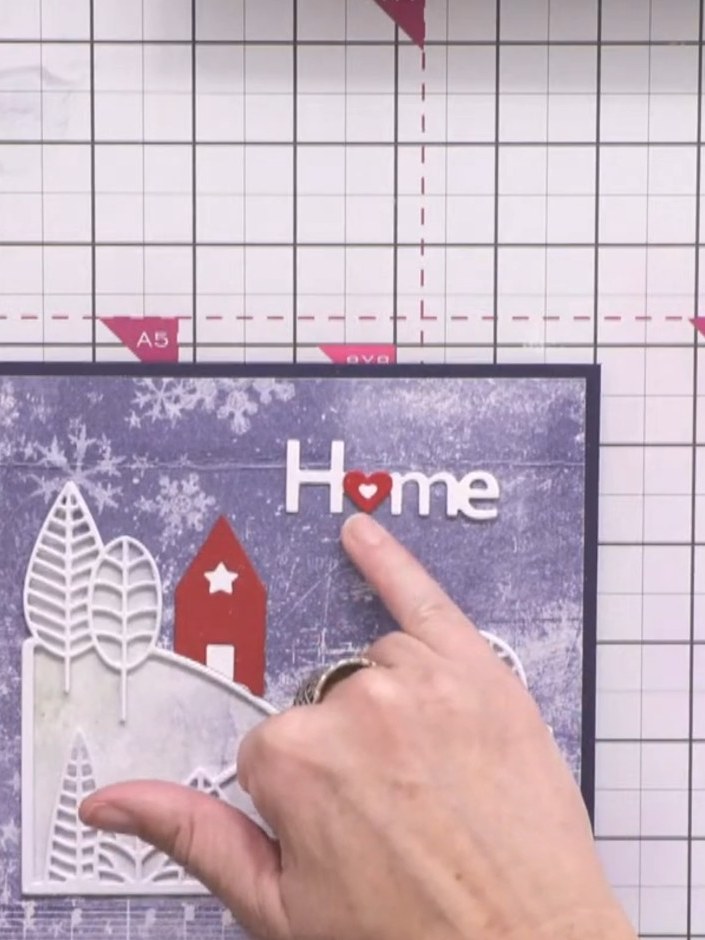 Step 12: Adhere the white 'Home' sentiment with the red heart accent to the centre top of the card. Add decorative whit