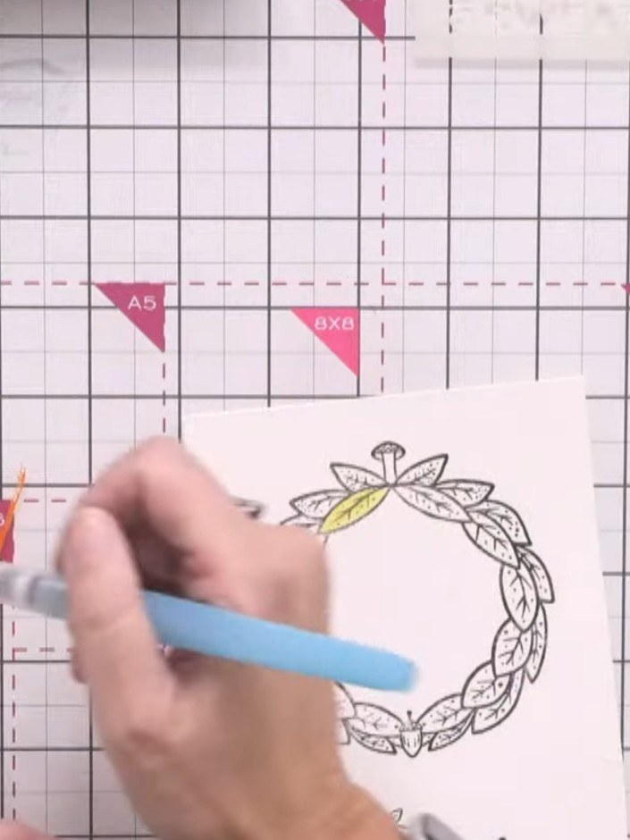 Passo 11: Colour the stamped wreath using distress oxide inks and a water brush. Blend autumn colours like oranges and y
