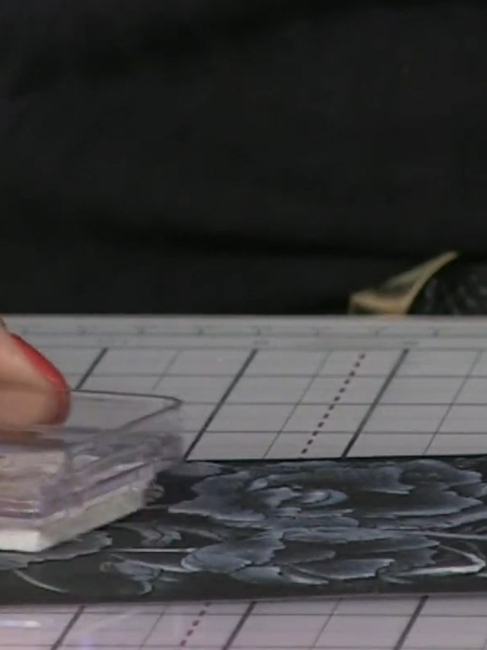 Passo 4: Gently rub the white ink pad across the raised embossed areas of the black card to highlight the floral design