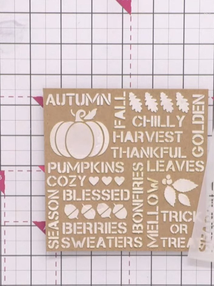 Passo 1: Apply white texture paste through the Autumn Days stencil onto kraft cardstock using a palette knife. Work the