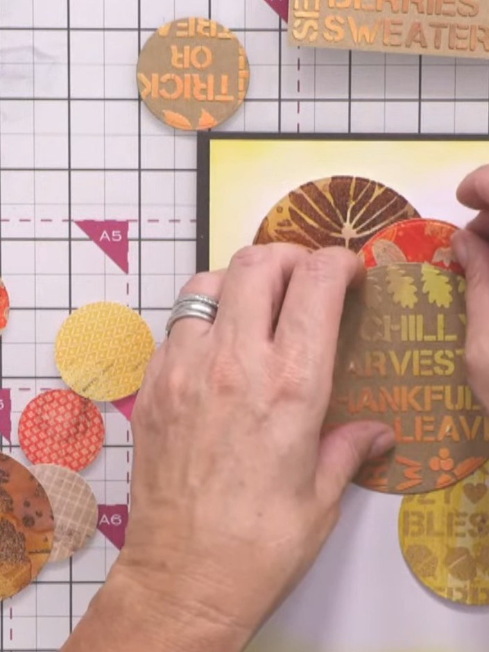 Passo 9: Mount the main focal circle onto the card using foam tape for added dimension. Position it centrally over the 