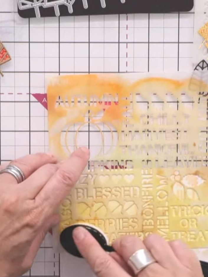Stap 6: Using the Autumn Days stencil, lightly apply yellow and orange ink to the background of your card panel. Work 
