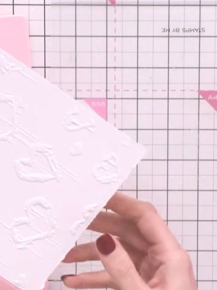 Step 4: Carefully lift the embossing folder away from the white cardstock to reveal the embossed floral heart pattern,