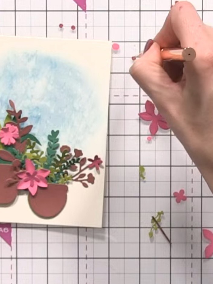 Step 12: Add eyeball centres to the pink flowers using a brown pen or marker. Embellish the card with gems, sequins or 
