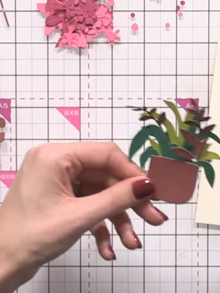 Step 9: Attach the pink flower die-cuts to the basket arrangement, positioning them at varying heights within and arou