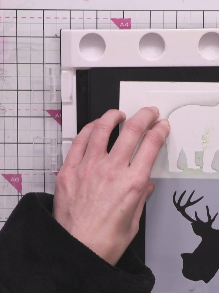 Step 9: Hold the bear stencil in place using a magnet on your magnetic glass mat. Using the tree stamps and black ink,
